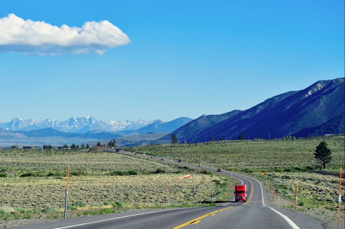 free-photo-of-a-red-truck-driving-down-a-highway-with-mountains-in-the-background